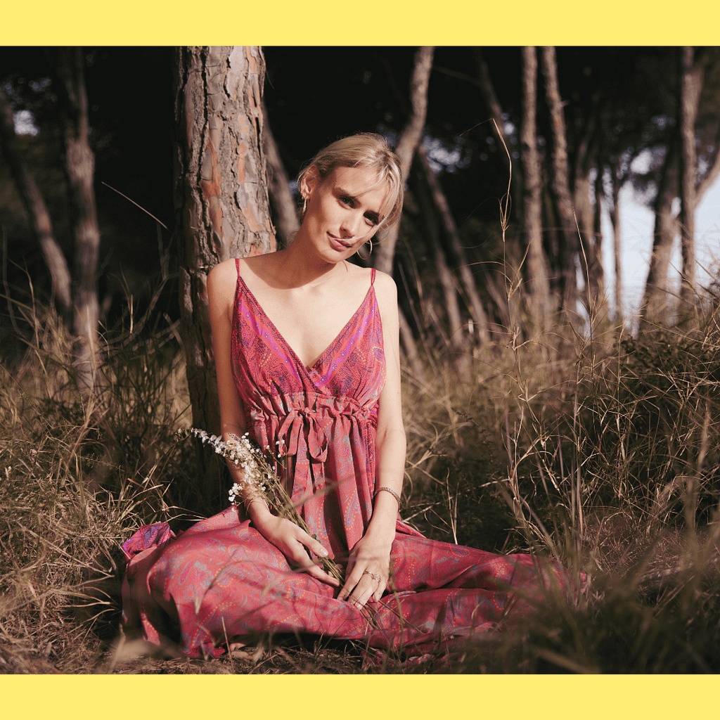 A blonde woman is sitting on the grass in a natural pink dress